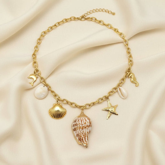 Gold necklace with shell and starfish charms against an ivory fabric background