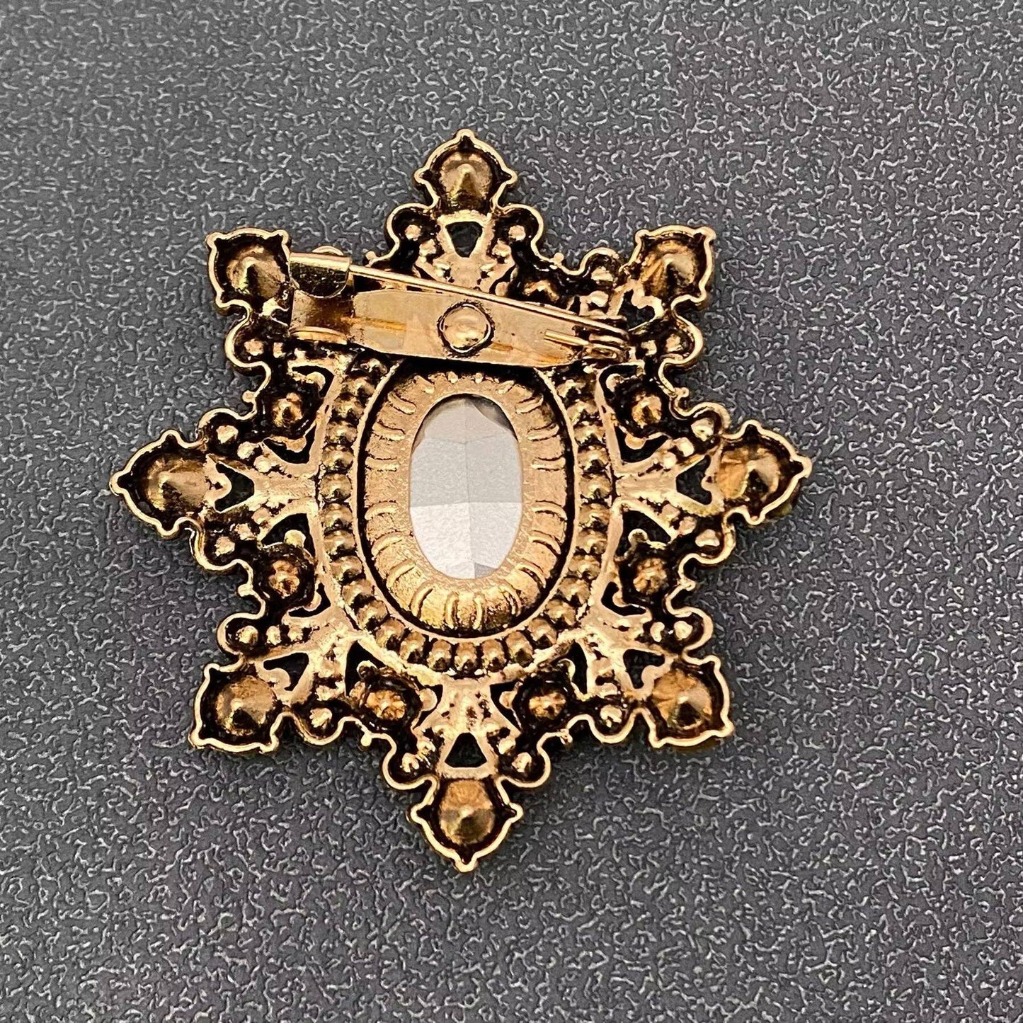 Back view of cognac crystal starburst brooch showing the pin closure against a grey textured background