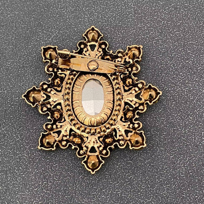 Back view of cognac crystal starburst brooch showing the pin closure against a grey textured background