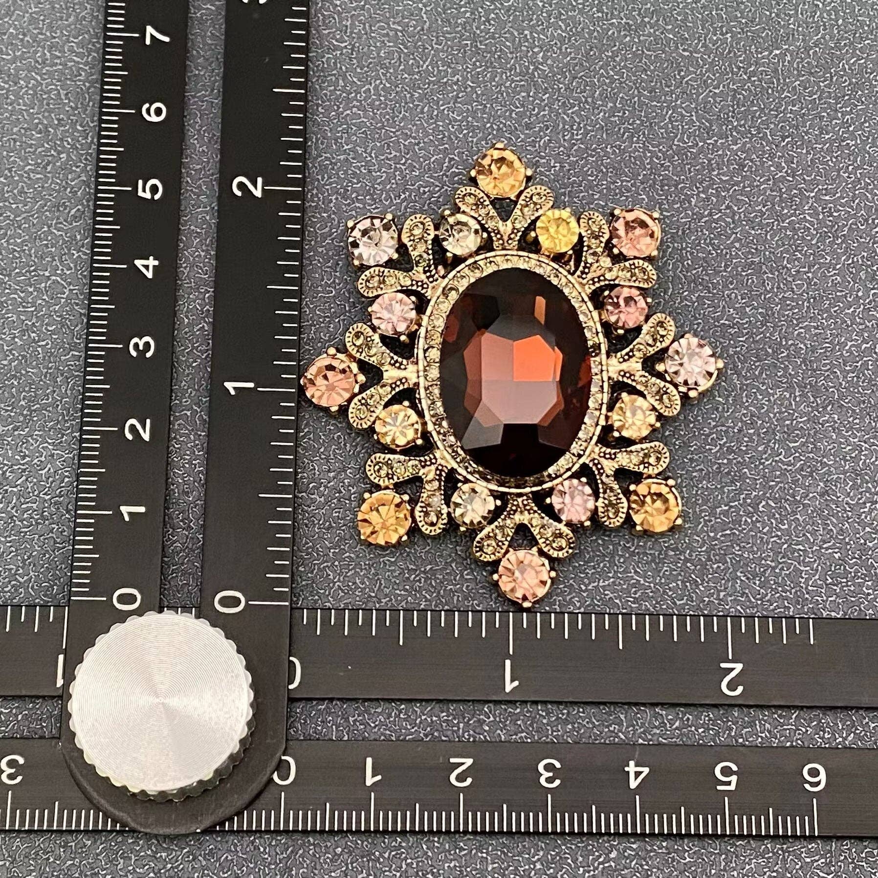 Cognac crystal starburst brooch next to a ruler for scale against a grey textured background