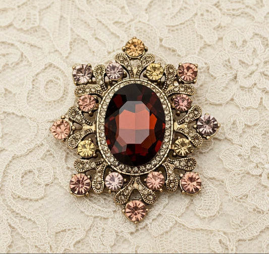 Cognac crystal starburst brooch with amber and rose rhinestones in gold filigree setting against a grey textured background by JuJu Loves