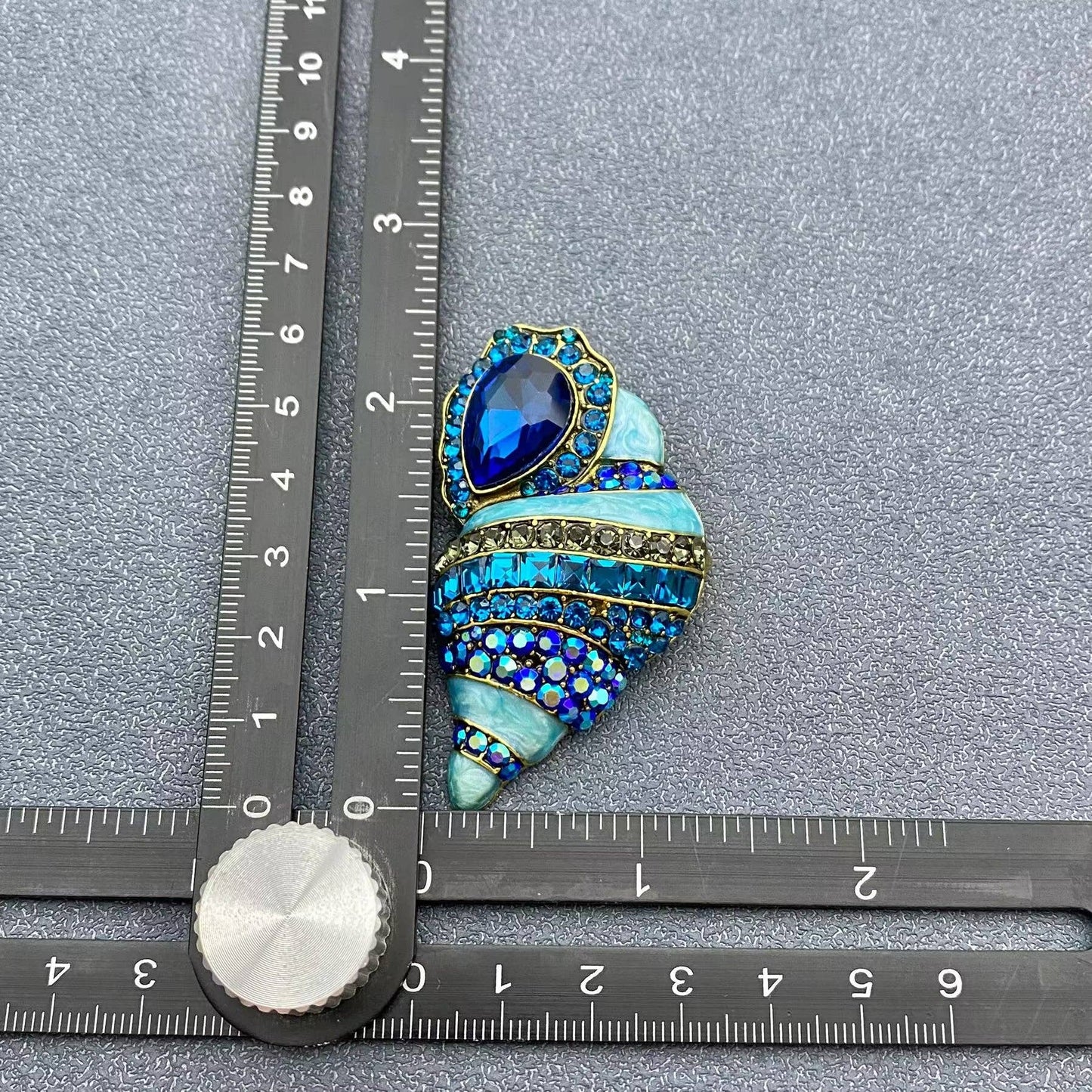 conch shell crystal brooch next to a ruler for scale on a grey background