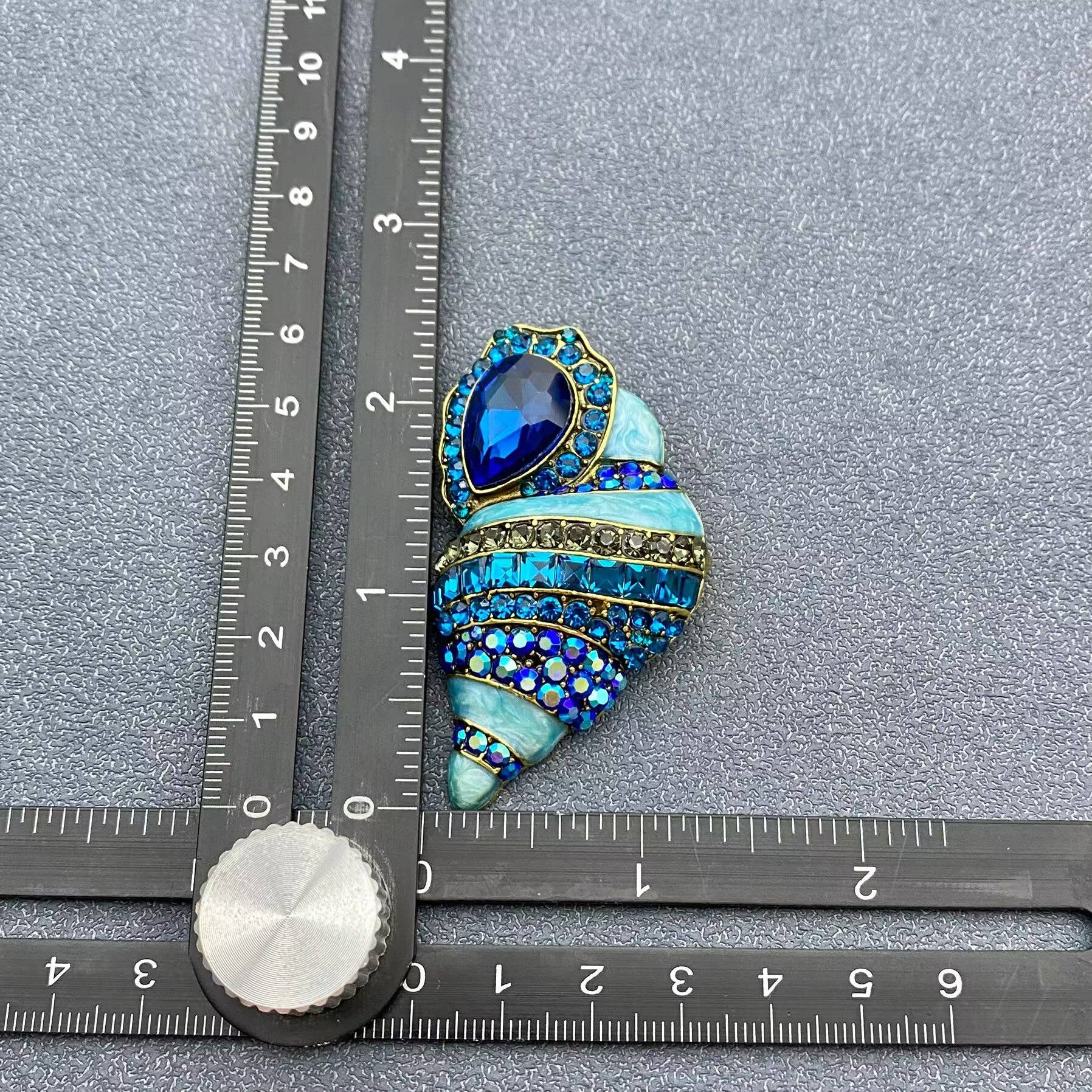 conch shell crystal brooch next to a ruler for scale on a grey background
