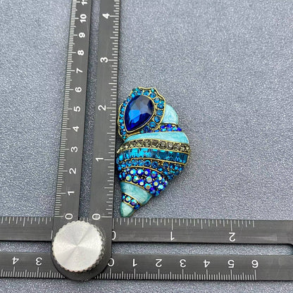 conch shell crystal brooch next to a ruler for scale on a grey background