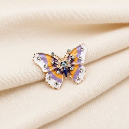 Butterfly-shaped brooch with purple and orange wings on an ivory fabric background