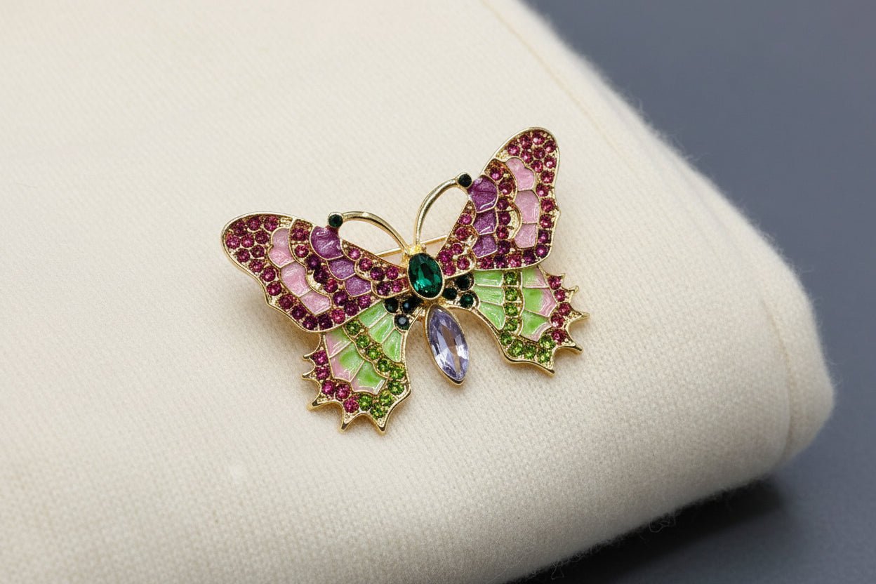 Butterfly-shaped brooch with gemstones laying on an ivory sweater against a grey background