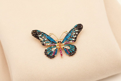 Butterfly-shaped brooch with colorful gemstones laying on an ivory sweater 