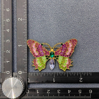 Butterfly-shaped brooch with gemstones on a gray background with a ruler for scale.