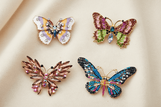 Four colorful butterfly brooches with gemstones on an ivory sweater fabric background