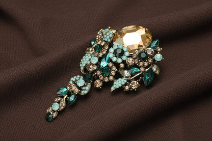 Decorative brooch with green and gold gemstones on a chocolate fabric background