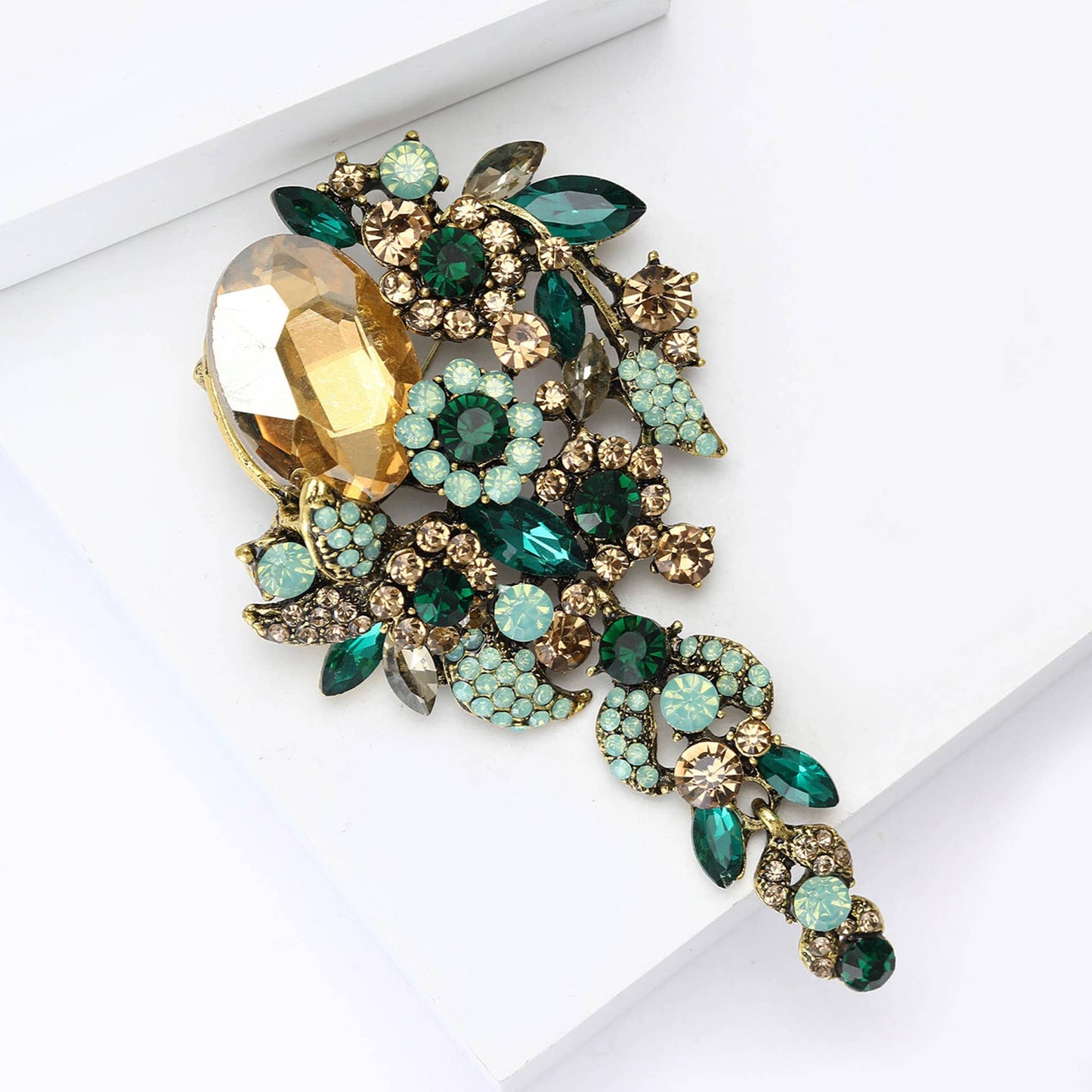 Cascade style brooch with green and amber crystals against a white background