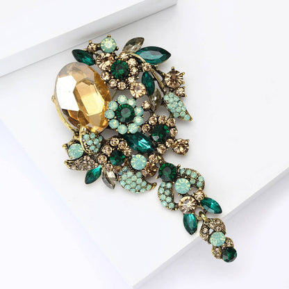 Cascade style brooch with green and amber crystals against a white background