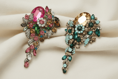 Two ornate cascade style brooches with colorful gemstones on an ivory sweater material background