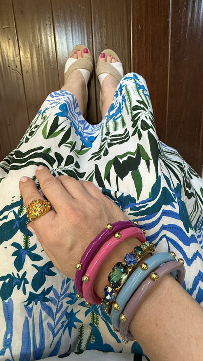 Person wearing a colorful patterned dress with floral design, and wearing multiple bracelets, a blue crystal cuff, and gold multi-colored gemstone dome ring