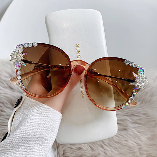 a woman's hand holding cyrstal embellished cat eye sunglasses and a white sunglass case against an ivory faux fur background