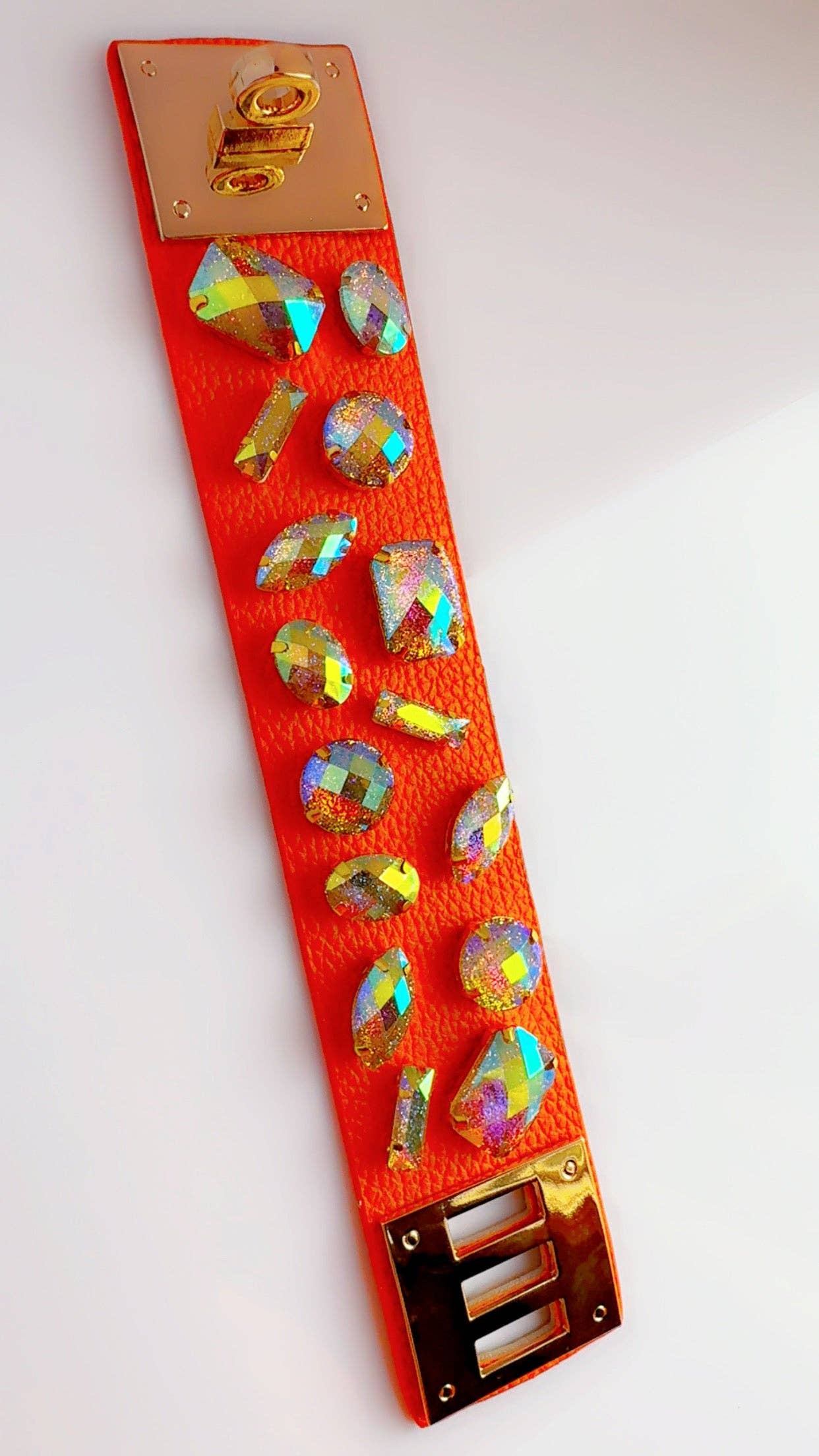 Orange leather cuff bracelet with colorful rhinestones laying flat on a white surface with a bird's eye view