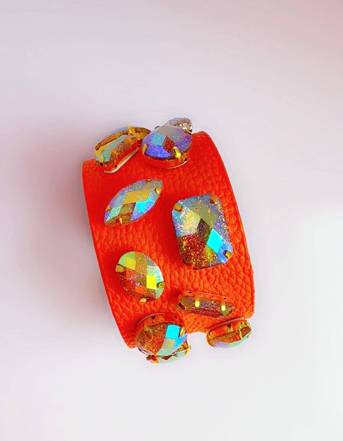 Orange leather cuff bracelet with colorful gemstones on a white surface