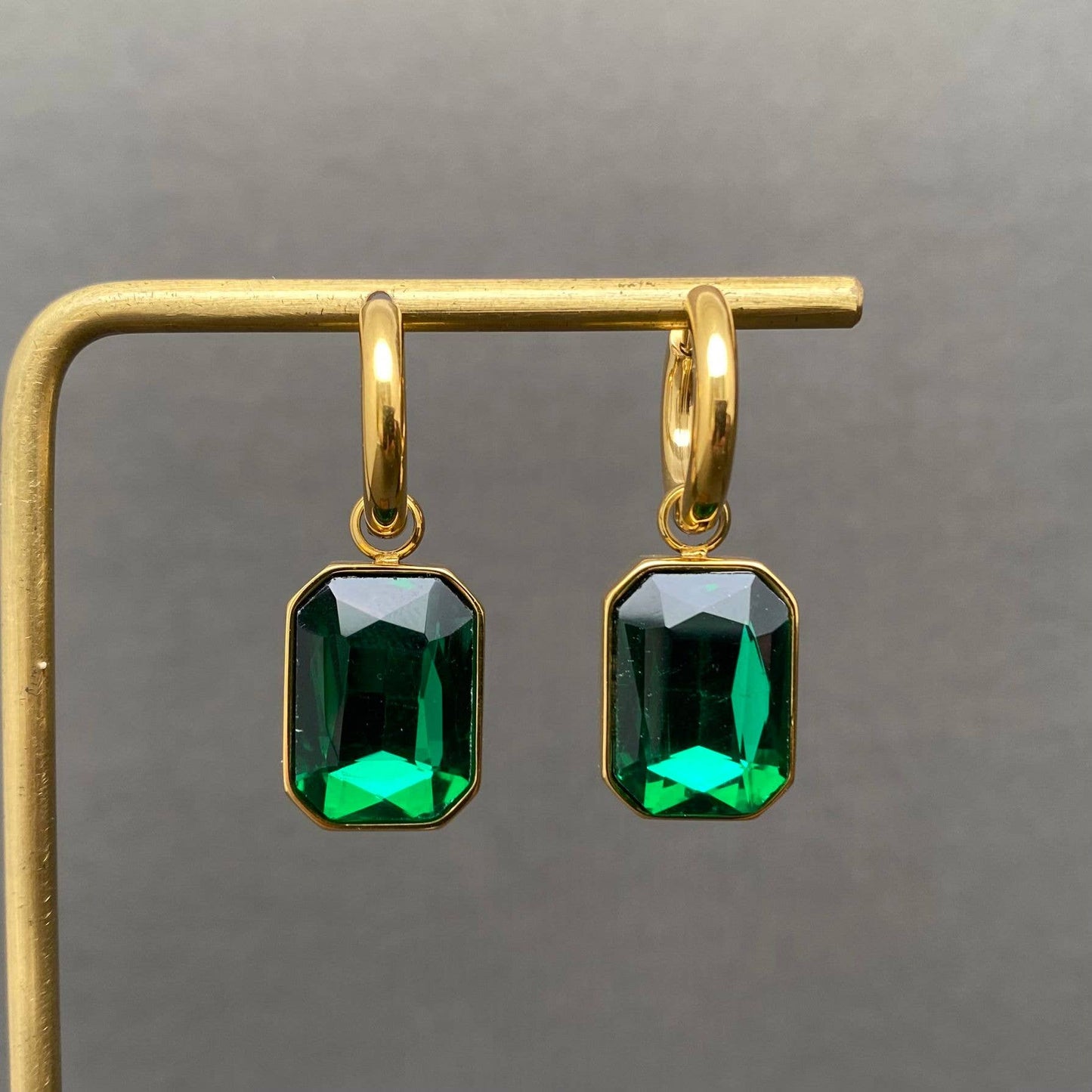 Gold earrings with green gemstones on a gray background