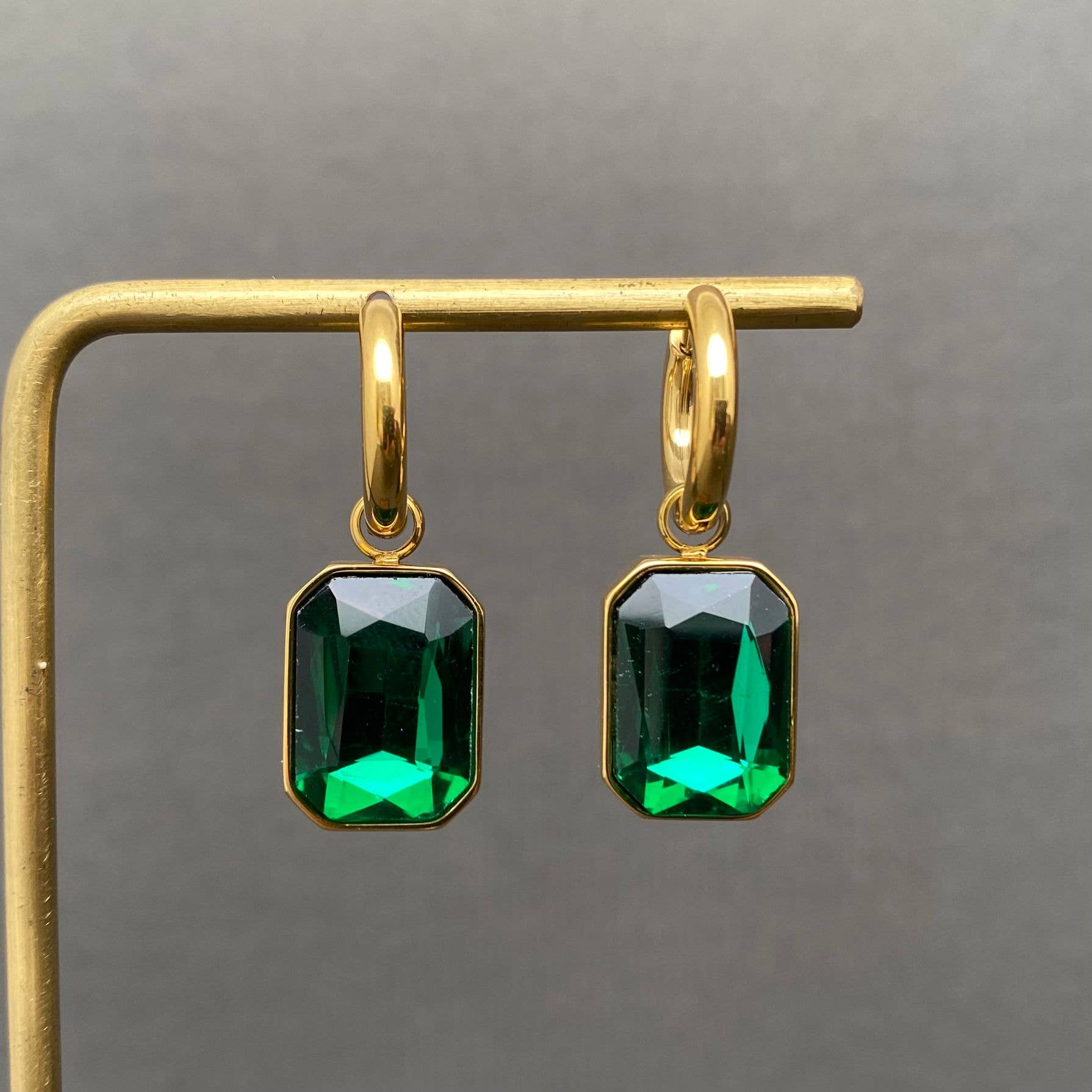 Gold earrings with green gemstones on a gray background