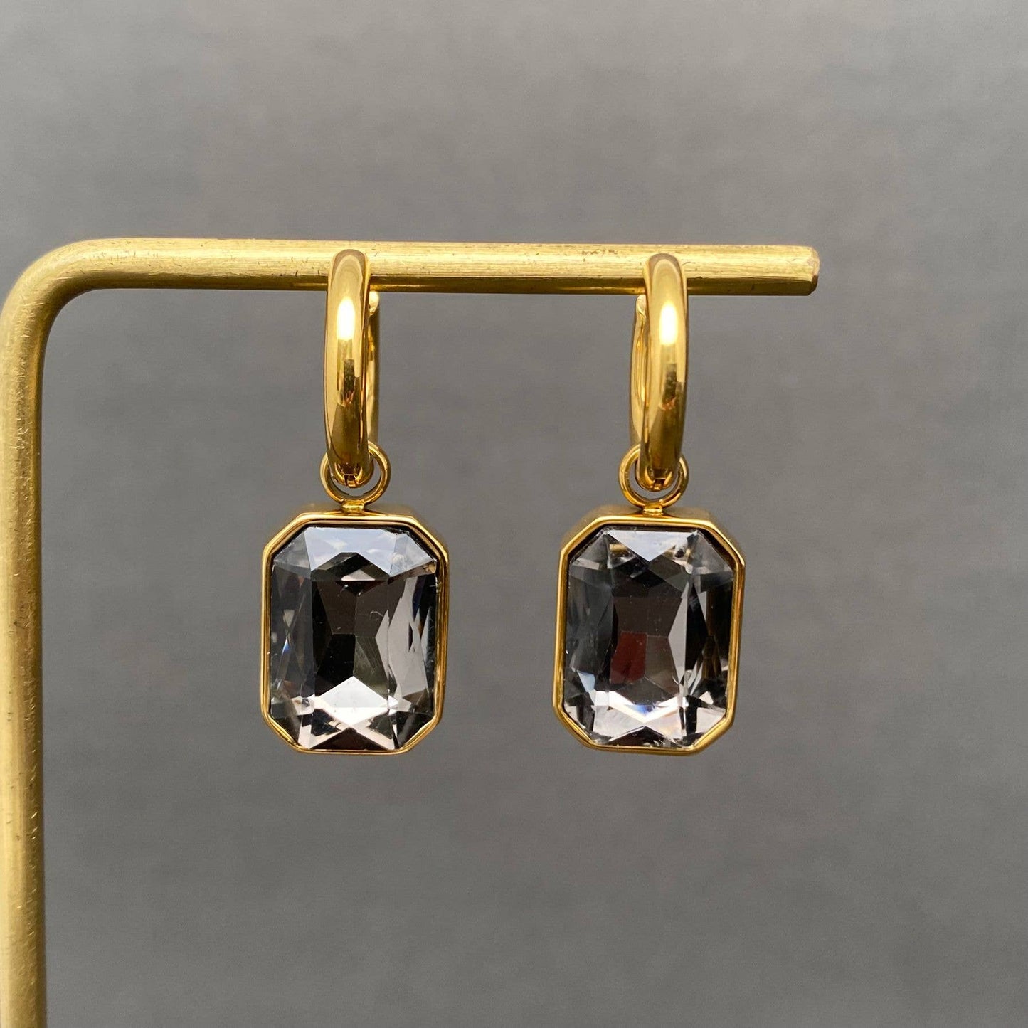 Gold earrings with rectangular grey gemstones on a gray background
