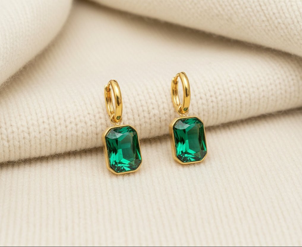 Gold earrings with green gemstones on an ivory sweater material background