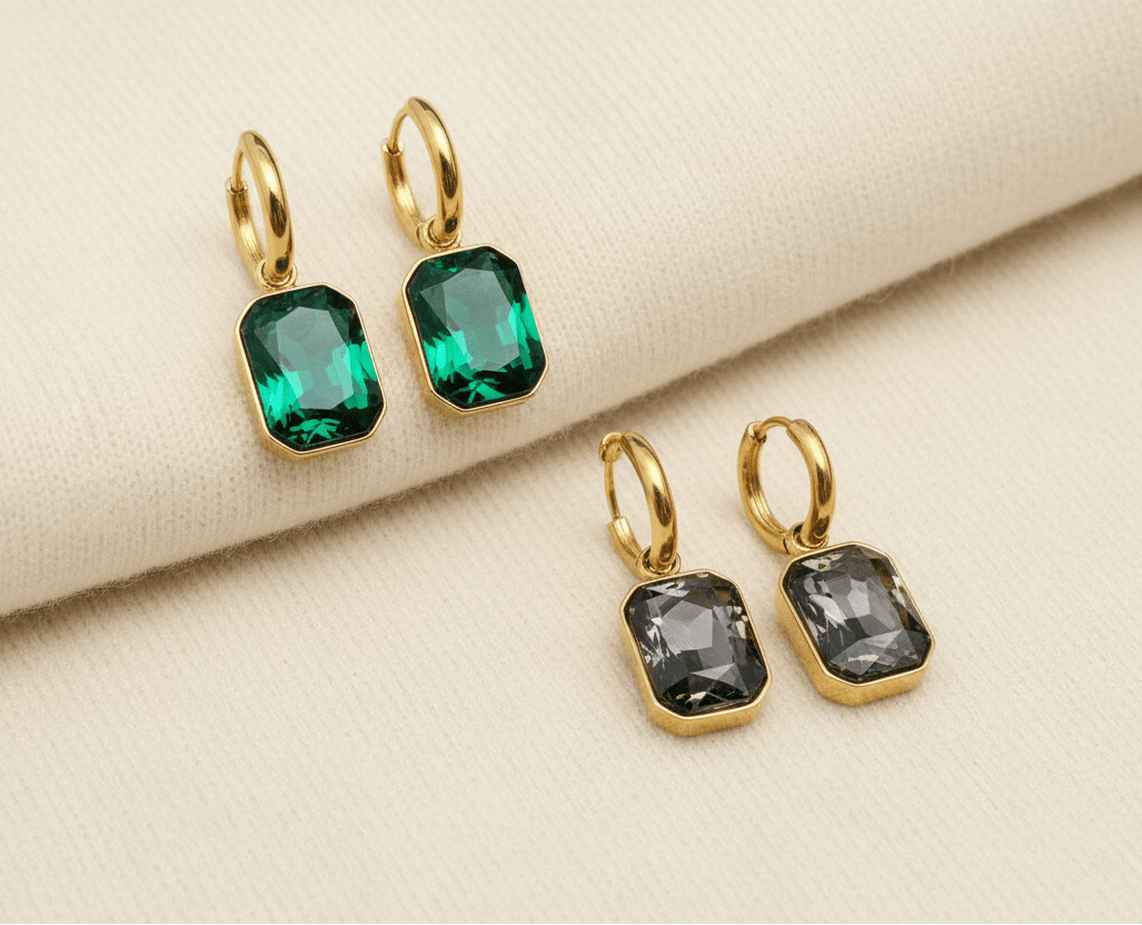 Gold hoop earrings with green and grey gemstones on an ivory sweater material background