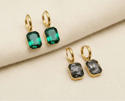 Gold hoop earrings with green and grey gemstones on an ivory sweater material background