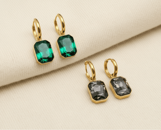 Gold hoop earrings with green and grey gemstones on an ivory sweater material background