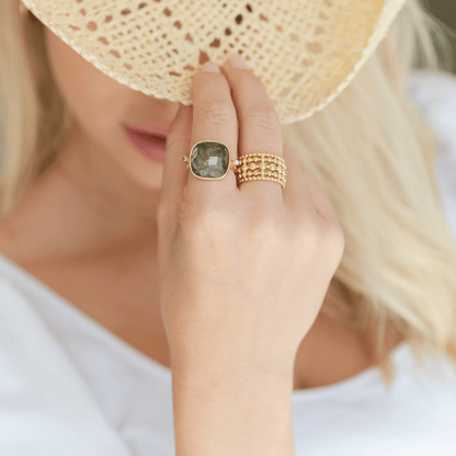 Close-up of a hand wearing a gold ring with a smokey gemstone and a gold ring, holding a straw hat.