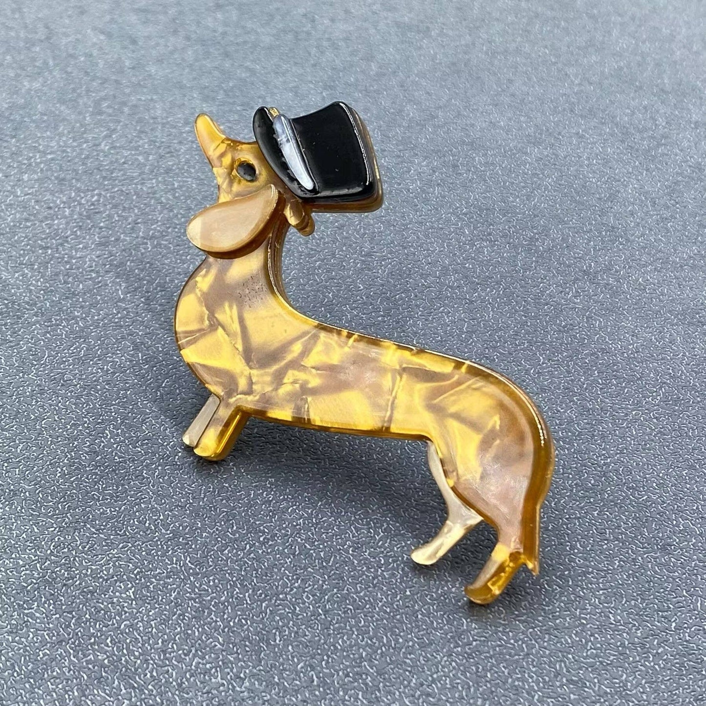 Dog-shaped brooch with a black top hat on a gray background