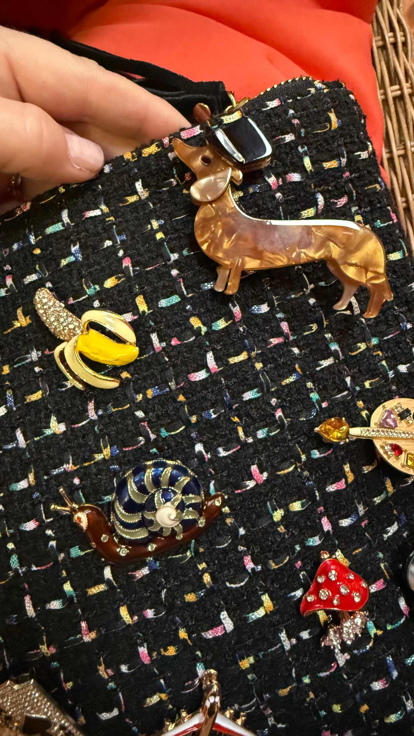 Dachshund brooch pinned on black textured handbag with other brooches