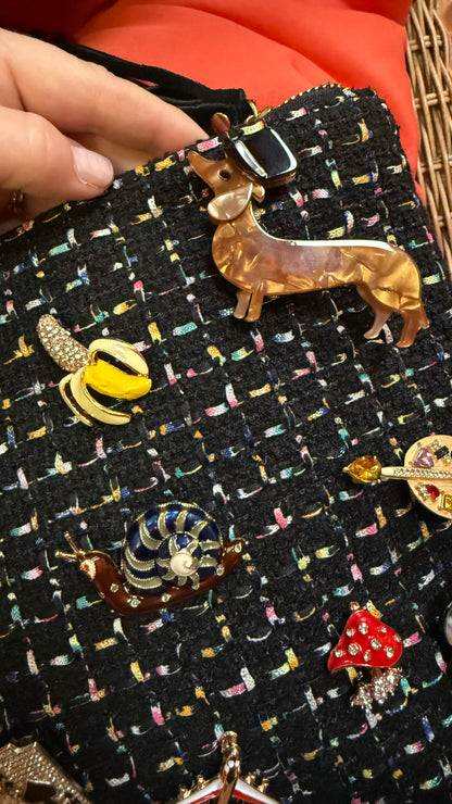 Dachshund brooch pinned on black textured handbag with other brooches