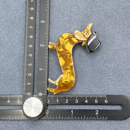 Gold-colored acrylic dog brooch with a black top hat on a gray background with a ruler for scale.