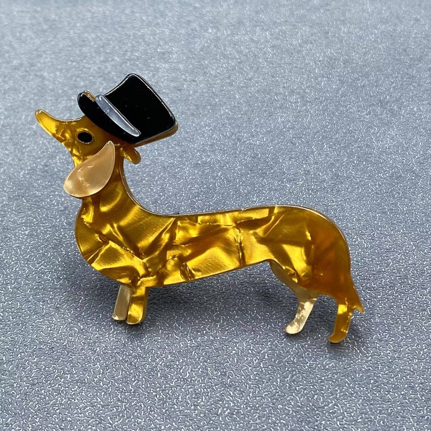 Gold acrylic dachshund dog brooch with a black top hat on a gray background