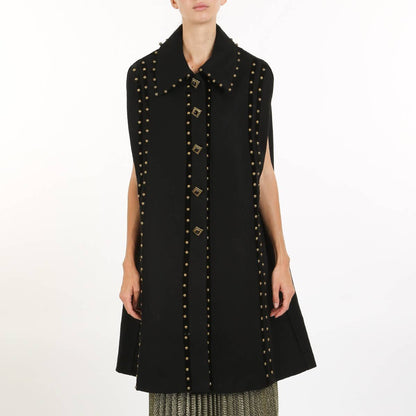 a woman wearing a black cape coat with gold stud details against a white background