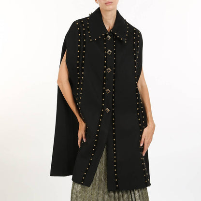 a woman wearing a black cape coat with gold stud detailing against a white background