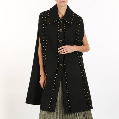 A model wearing a black studded cape with a wide collar and round shoulder pads against a white background.
