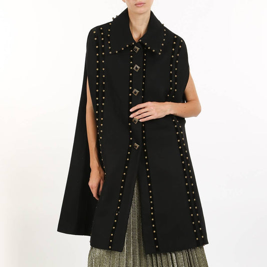 A model wearing a black studded cape with a wide collar and round shoulder pads against a white background.