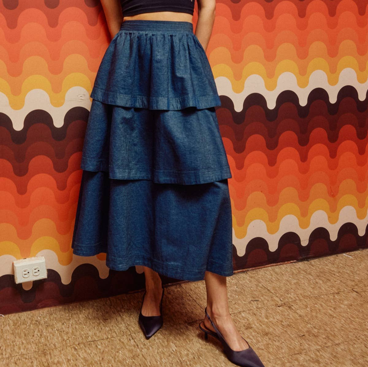 woman in black heels wearing denim tiered midi skirt in front of geometric wall