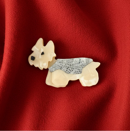 A white Yorki dog themed acrylic brooch on a red wool fabric background