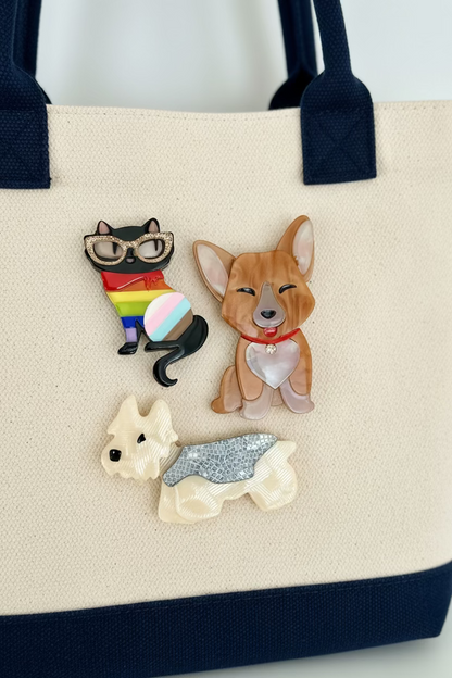 Three acrylic brooches on a canvas bag with navy blue trim including a cat, corgi, and yorki