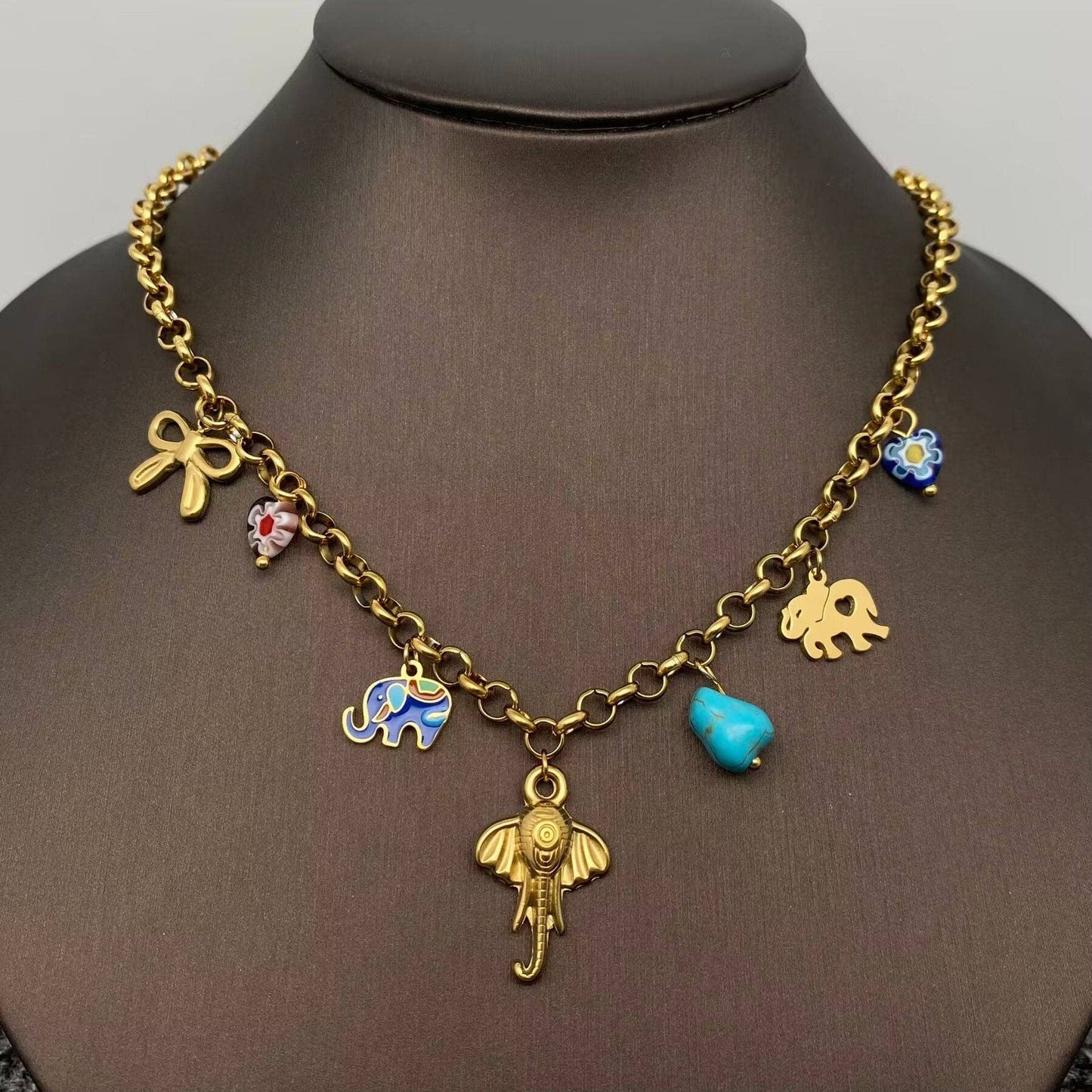 gold multi charm necklace with elephants, bow, and turquoise charms hanging on a black necklace stand