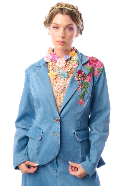 a woman wearing a blue denim blazer with floral embroidery against a white background