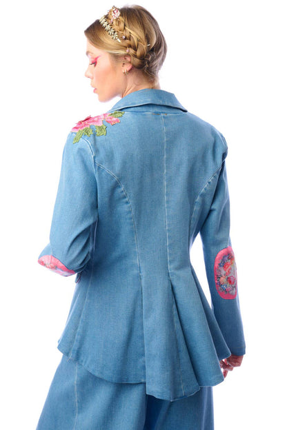 Back view of a woman wearing a blue denim blazer with floral embroidery against a white background