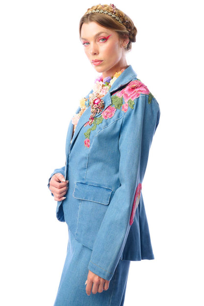 Side view of a woman wearing a blue denim blazer with floral embroidery against a white background