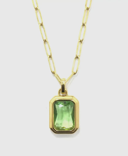 close up of emerald colored stone set in gold against a white background