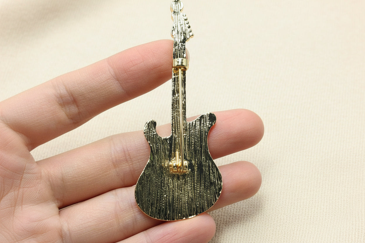 back view of guitar shaped brooch to show the pin closure held in a hand against a grey background