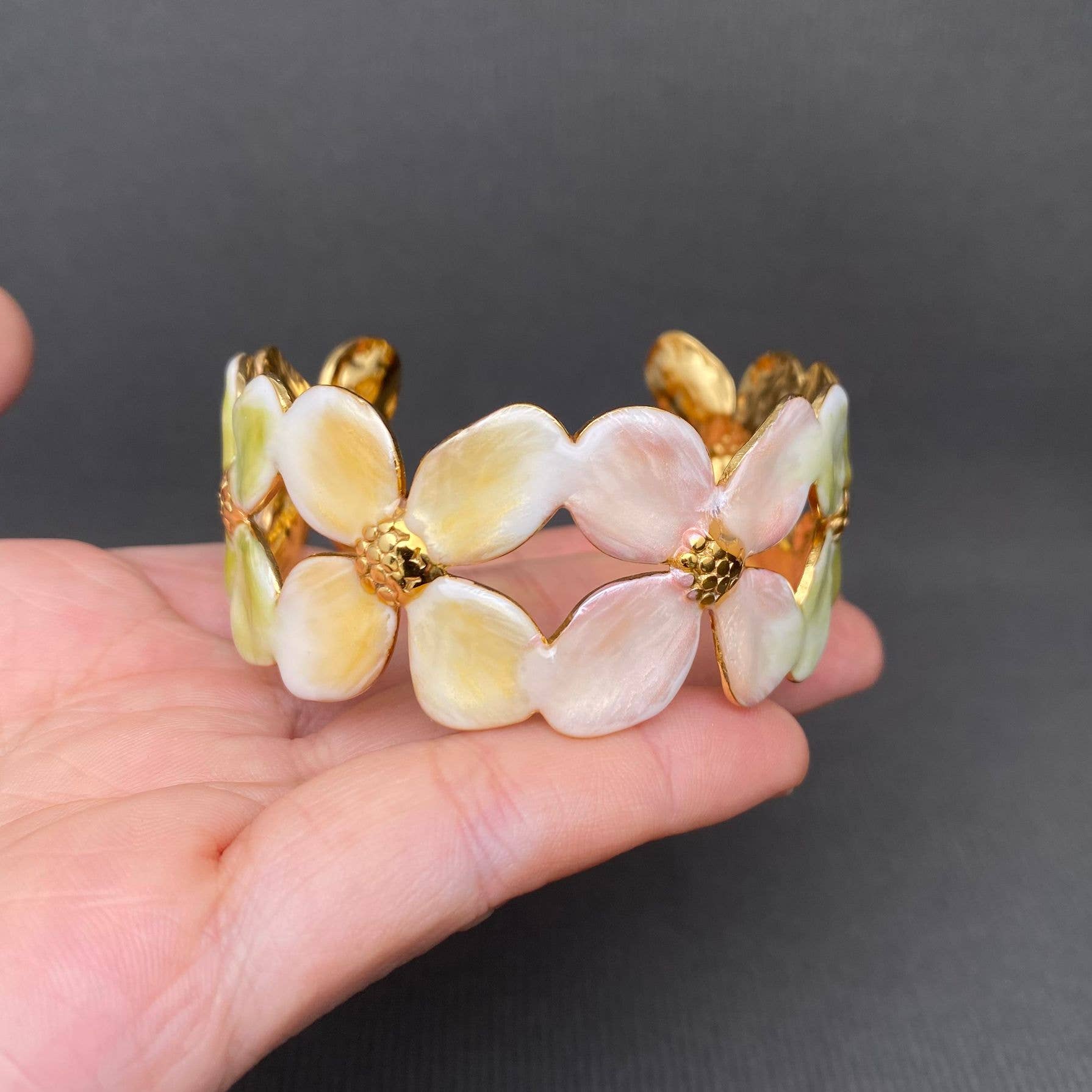 Floral bracelet with gold accents held in a hand against a dark background