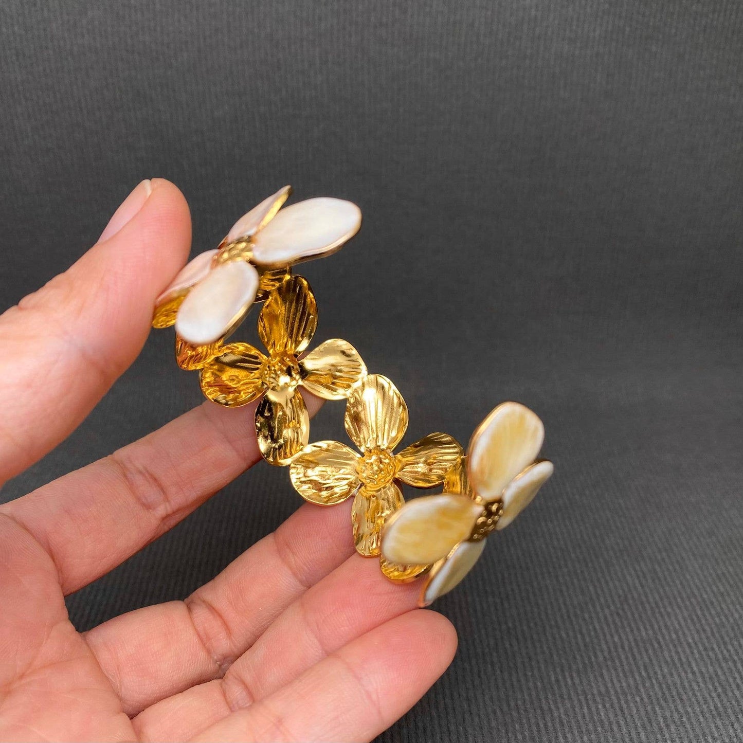 Gold and beige floral cuff bracelet held in a hand against a dark background
