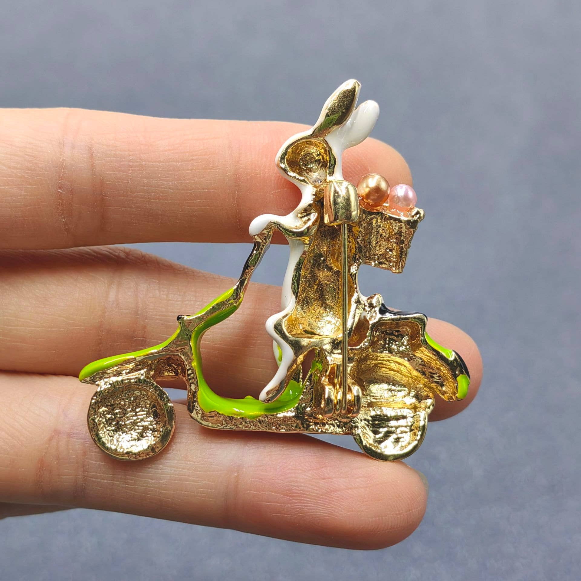Back view of rabbit on a scooter brooch to show pin closure in a hand against a gray background